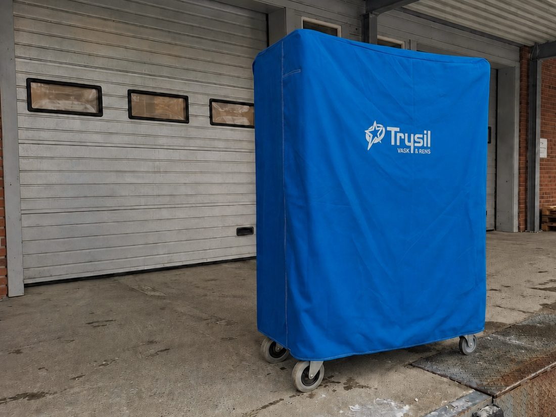Hyllevogn med blått tekstilvogntrekk ved lasterampen på et vaskeri.